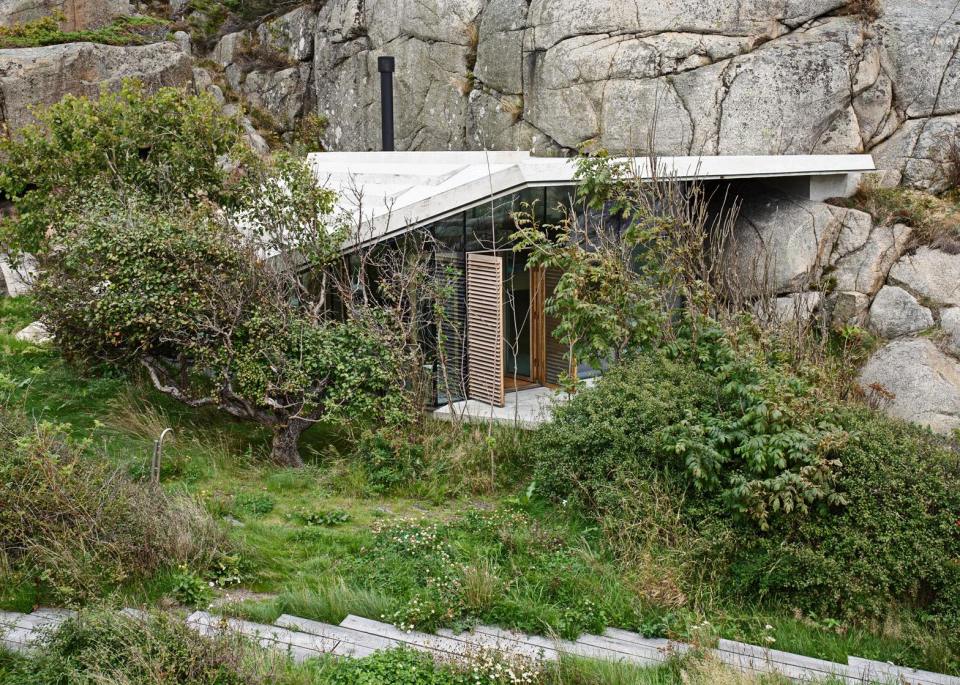 Half-hidden by dense vegetation, this modern cabin is tucked into a rocky Norwegian coastline. It is a 323 sq ft studio design with a sleeping loft suspended from the ceiling. | www.facebook.com/SmallHouseBliss