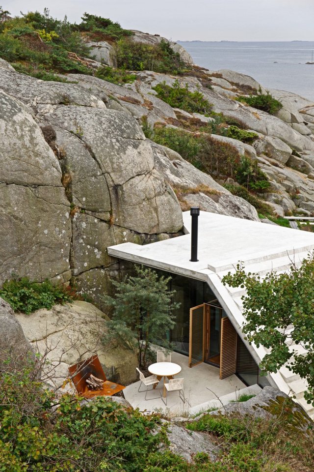 Half-hidden by dense vegetation, this modern cabin is tucked into a rocky Norwegian coastline. It is a 323 sq ft studio design with a sleeping loft suspended from the ceiling. | www.facebook.com/SmallHouseBliss